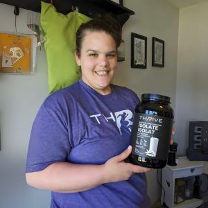 Smiling customer indoors holding Thrive Whey Protein Isolate