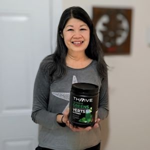 Woman holding Thrive Ultimate Greens tub and smiling indoors