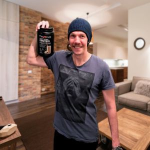 Man holding Thrive Protein in a wood-panelled room