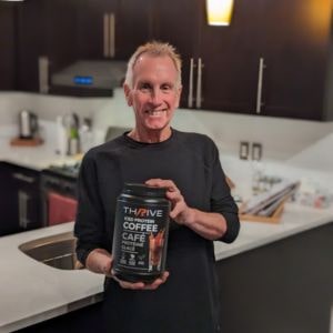 Older customer in kitchen holding Thrive Protein Coffee and smiling