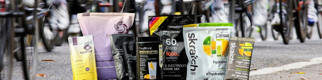 Electrolyte and carbohydrate drink mixes including Skratch Labs, Precision Hydration, Tailwind, Maurten, and Thrive EnduraFuel displayed at an endurance cycling event